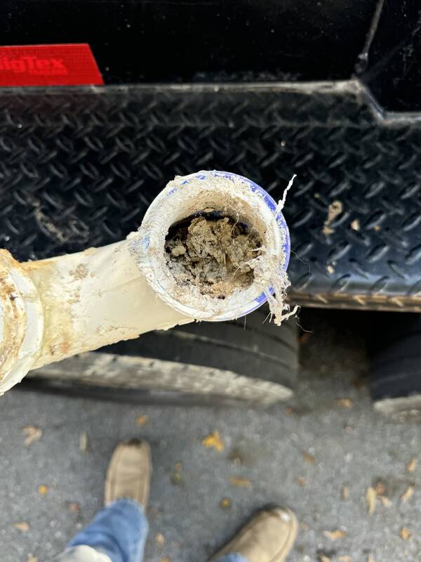 Cut section of white drain pipe packed with built-up grease and debris, held beside a diamond-plate truck step